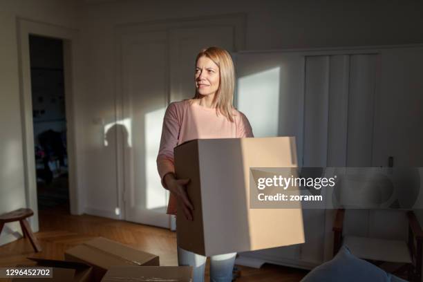 frau zieht ein und trägt eine kiste in ihrer neuen wohnung - boxes home stock-fotos und bilder