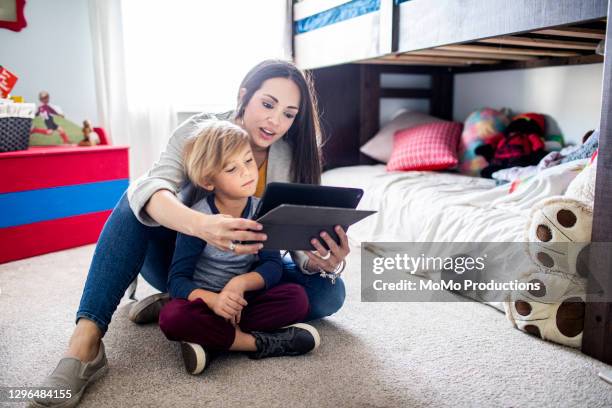 mother and son watching smart device together - mutter tablet zuhause stock-fotos und bilder