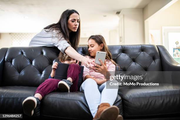 mother monitoring children using smart devices on sofa at home - parental control stock-fotos und bilder