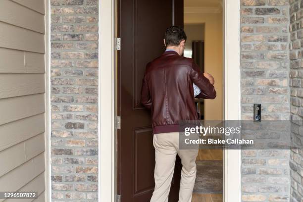 male entering the home with back to camera and wide view of home exterior - welcome home stock pictures, royalty-free photos & images