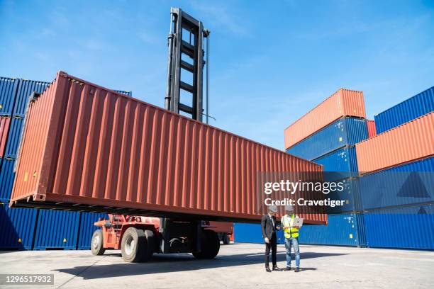 engineers holding laptop checking shipping cargo freights in front of cargo containers in shipping container yard. - safe harbor stock pictures, royalty-free photos & images