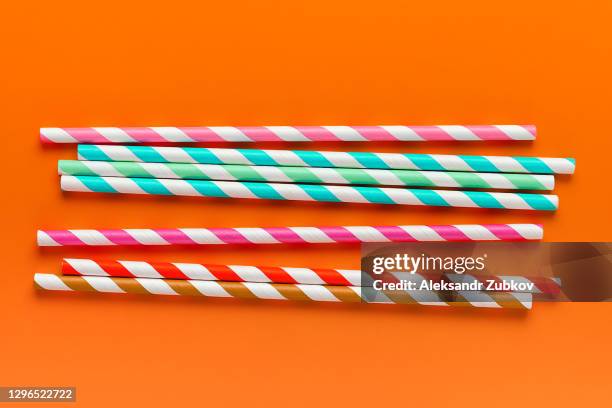 multi-colored, reusable, paper, striped straws for drinking juice or cocktail on a bright orange background. - striped straw stock pictures, royalty-free photos & images