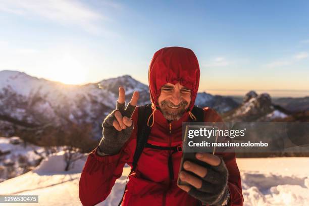 hiker on mountain during video call with smartphone - winter adventure stock pictures, royalty-free photos & images