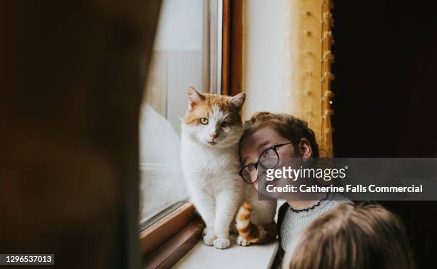 young girl with glasses looks up lovingly towards her cat, and leans her head against him. - pets foto e immagini stock