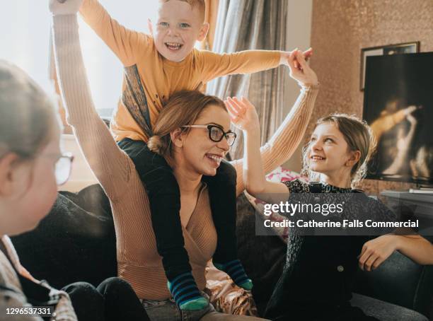 mother with son on her shoulders, is surrounded by her happy children - kid mess child stock-fotos und bilder