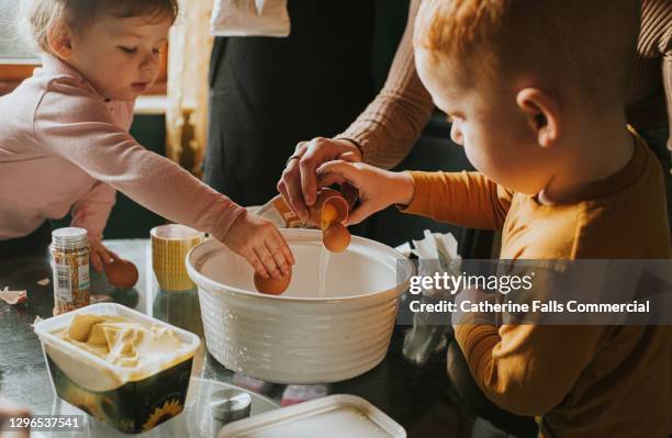 children cracking eggs into a mixing bowl - children cooking stock-fotos und bilder