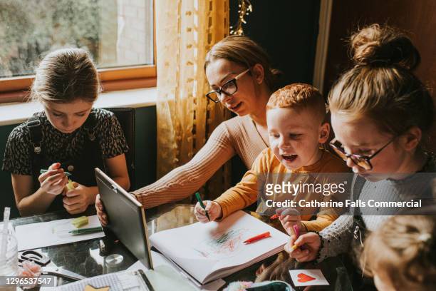 mother homeschooling her children while using a digital tablet - men women & children film stock-fotos und bilder