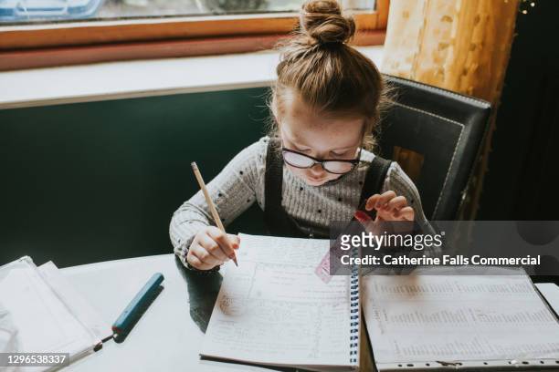 little girl sits at a kitchen table and does her homework / home schooling - hausaufgaben stock-fotos und bilder