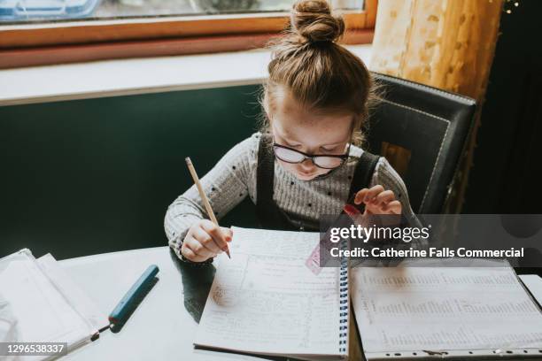 little girl sits at a kitchen table and does her homework / home schooling - young girls homework stock pictures, royalty-free photos & images