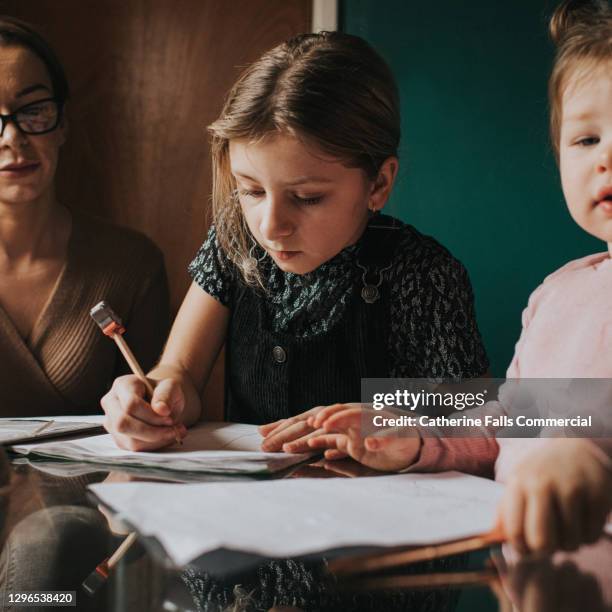little girl sits at a kitchen table and does her homework / home schooling - leanincollection stock pictures, royalty-free photos & images