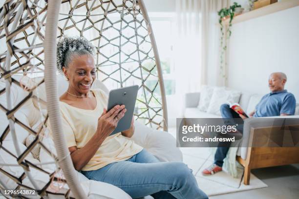 hoger paar in woonkamer, het boek van de mens dat en de vrouw leest gebruikend digitale tablet - african american woman with tablet stockfoto's en -beelden
