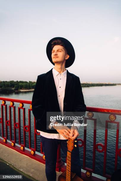 smiling young man walking on the bridge holding a guitar in his hands. - beach music festival photos et images de collection