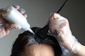 Closeup woman hands dyeing hair using black brush. Middle age woman colouring dark hair with gray roots at home