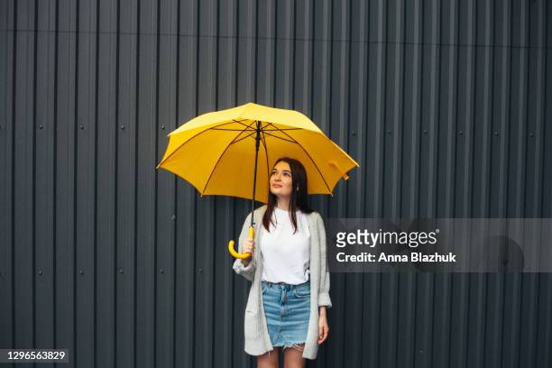 young woman holding big yellow umbrella in rainy day, dark gray wall background. trendy 2021 pantone colors: ultimate gray and illuminating yellow. - umbrella 個照片及圖片檔