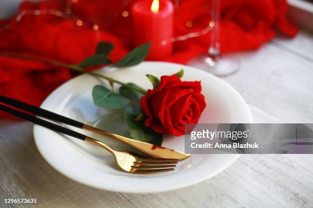 white plate with black and gold colored knife and fork and red rose flowers, candle and glass, white wood background. romantic greeting card for valentine's day. - valentines day dinner stock pictures, royalty-free photos & images