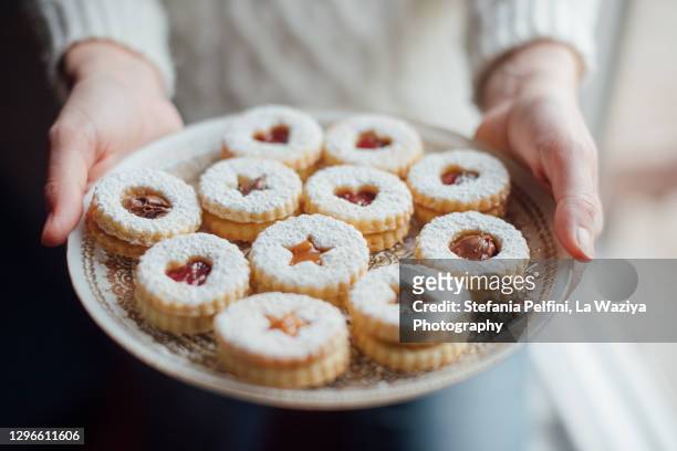 hands holding a plate with homemade linzer cookies - valentine's day holiday stock-fotos und bilder