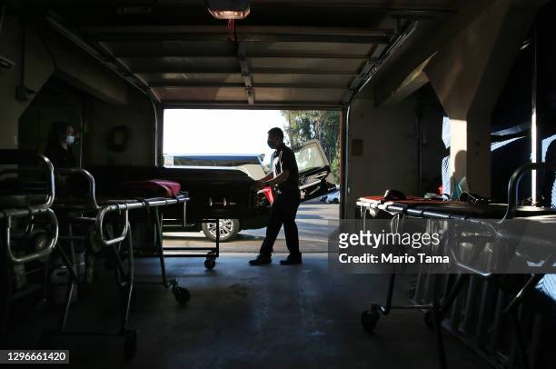 Funeral attendant Sam Deras helps wheel the casket of a person who died after contracting COVID-19 past gurneys toward a hearse at East County...