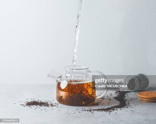 water pours into a glass teapot with black tea on a gray table with a can of dry tea. - tea can stock pictures, royalty-free photos & images