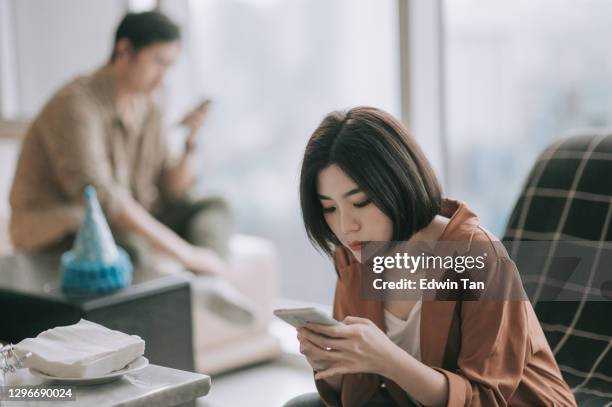 深刻な表情で離れて座ってリビングルームで電話を使用して不快なアジアの中国のカップル - 対立 ストックフォトと画像