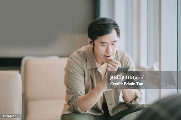 asian chinese man sitting on sofa living room using smart phone surf the net - cell phone confused stock pictures, royalty-free photos & images