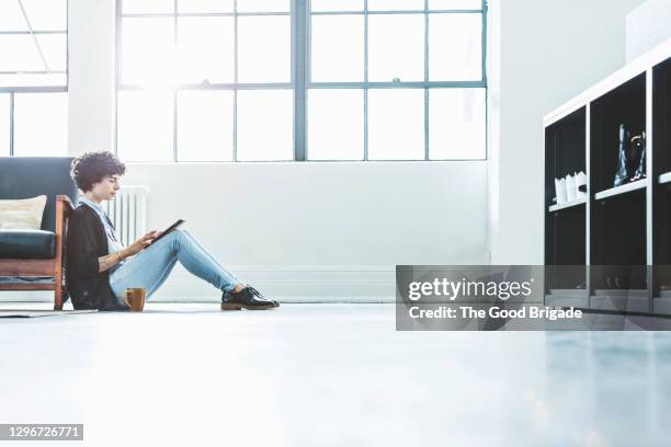 side view of businesswoman using digital tablet while sitting on floor at creative office - sitting on floor bildbanksfoton och bilder