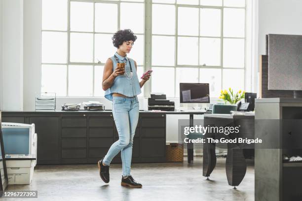woman looking at smart phone while walking in creative office - man walking phone stock-fotos und bilder