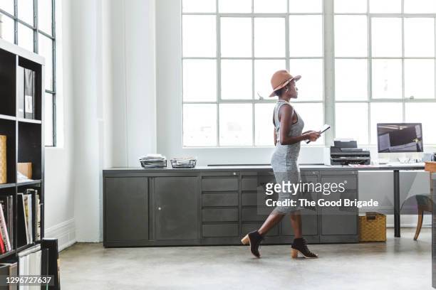full length side view of fashionable businesswoman holding digital tablet while walking at creative workplace - a la moda stock pictures, royalty-free photos & images