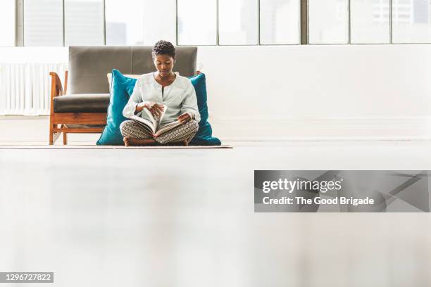 mid adult woman reading book in loft apartment - fashion woman floor cross legged stock pictures, royalty-free photos & images