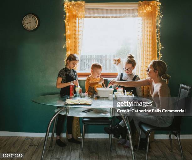 children baking at a table with mum supervising - cat bored stock-fotos und bilder