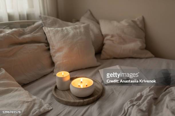 scented candles in ceramic bowls on linen bed with book at home. - cosy stock-fotos und bilder