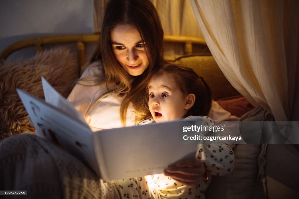 Mother and child reading book in bed before going to sleep