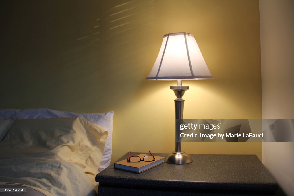 Bedroom night table with lamp, book and reading glasses