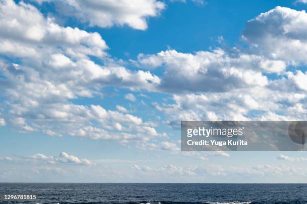 white clouds in a blue sky over a sea - fonds de nuage photos et images de collection