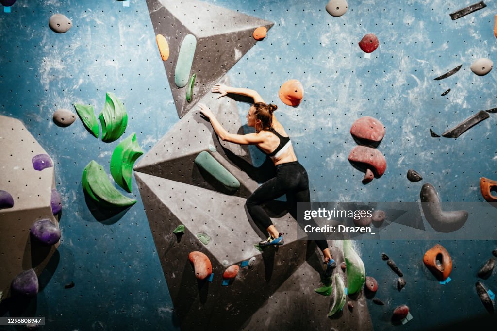 Strong woman climbing on boulder wall, wide angle photo