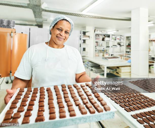 trabajador de la fábrica de chocolate sonriente sosteniendo una bandeja de golosinas recién hechas - fábrica de chocolate fotografías e imágenes de stock