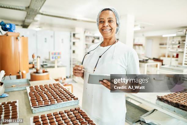 trabajador sonriente usando una tableta digital en una fábrica comercial de chocolate - fábrica-de-chocolate fotografías e imágenes de stock