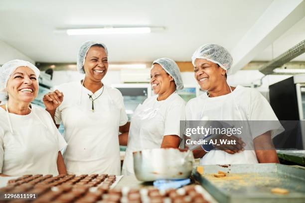 group of confectioners working laughing together in a chocolate factory - chocolate factory stock pictures, royalty-free photos & images