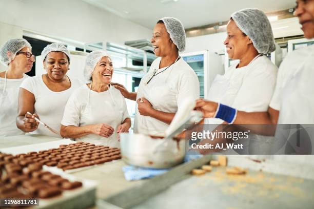 groep banketbakkers die samen lachen terwijl het werken in een chocoladefabriek - chocolate factory stockfoto's en -beelden