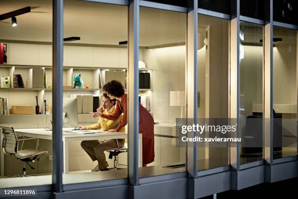 corporate professionals working late in modern office - downlight stock pictures, royalty-free photos & images