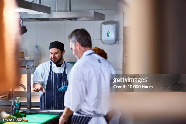 chef discussing with team in commercial kitchen - kochlehrling stock-fotos und bilder
