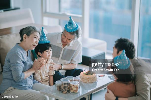 aziatische chinese multi generatie familie klappen handen en zingen verjaardagslied vieren verjaardag voor 6 jaar oude jongen in woonkamer - chinese birthday stockfoto's en -beelden