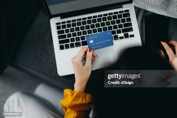 overhead view of young asian woman sitting on the floor by the sofa, shopping online with laptop and entering credit card details for payment at home. technology makes life so much easier - shopaholic stock pictures, royalty-free photos & images