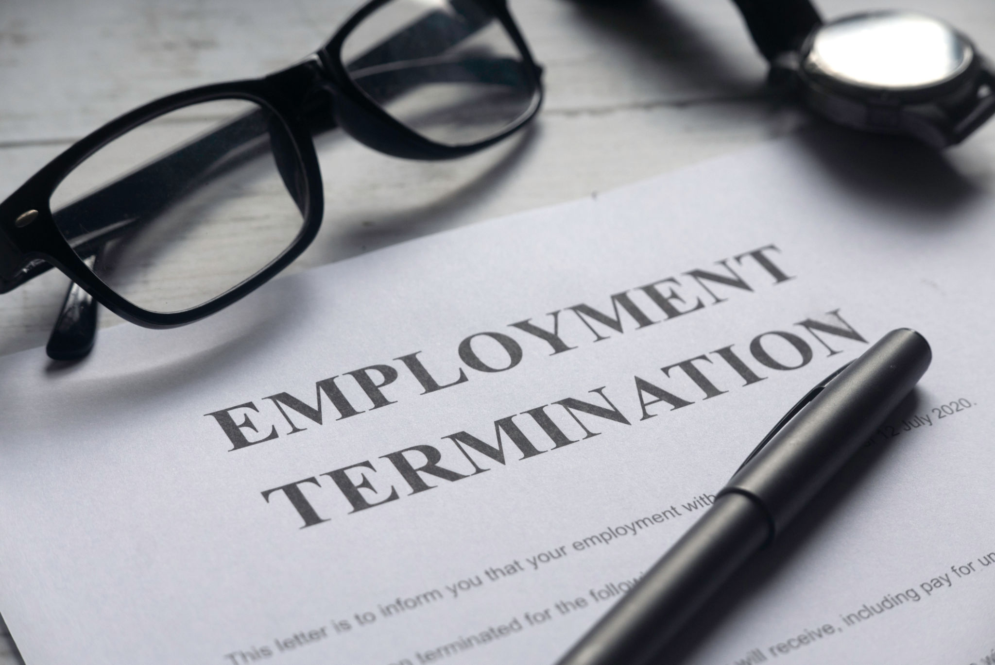 Selective focus of glasses,watch,pen and Employment Termination letter on a white wooden background. Selective focus of glasses,watch,pen and Employment Termination letter on a white wooden background.