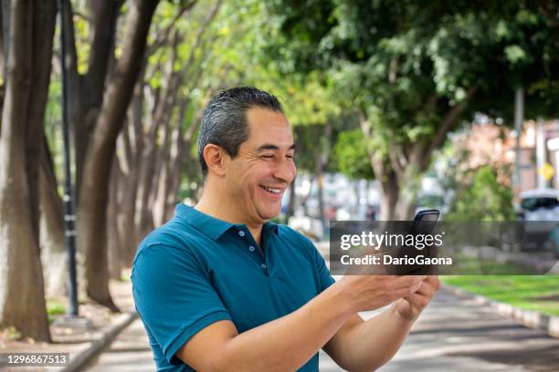 hombre en el parque viendo celular - mid adult men fotografías e imágenes de stock