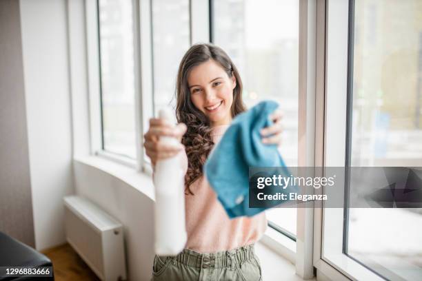 linda jovem sorridente limpando e limpando janela com garrafa de spray e pano - mop - fotografias e filmes do acervo