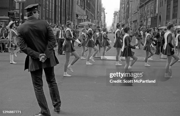 View of an officer with the New York Police Department standing guard, as a high school marching band goes by on 5th Avenue during the Columbus Day...