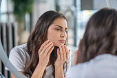 Young adult woman looking at face in mirror