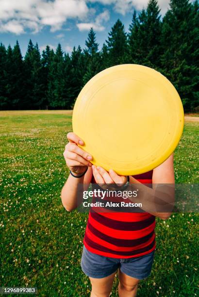 young girl hiding behind a yellow frisbee in playing field - disc golf stock pictures, royalty-free photos & images