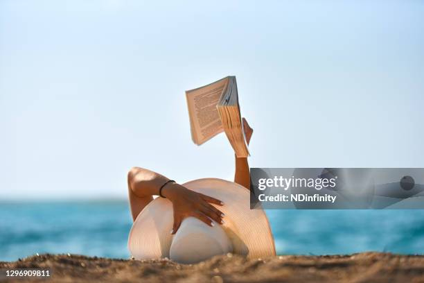 joven lee un libro en la foto de la playa - descansar fotografías e imágenes de stock