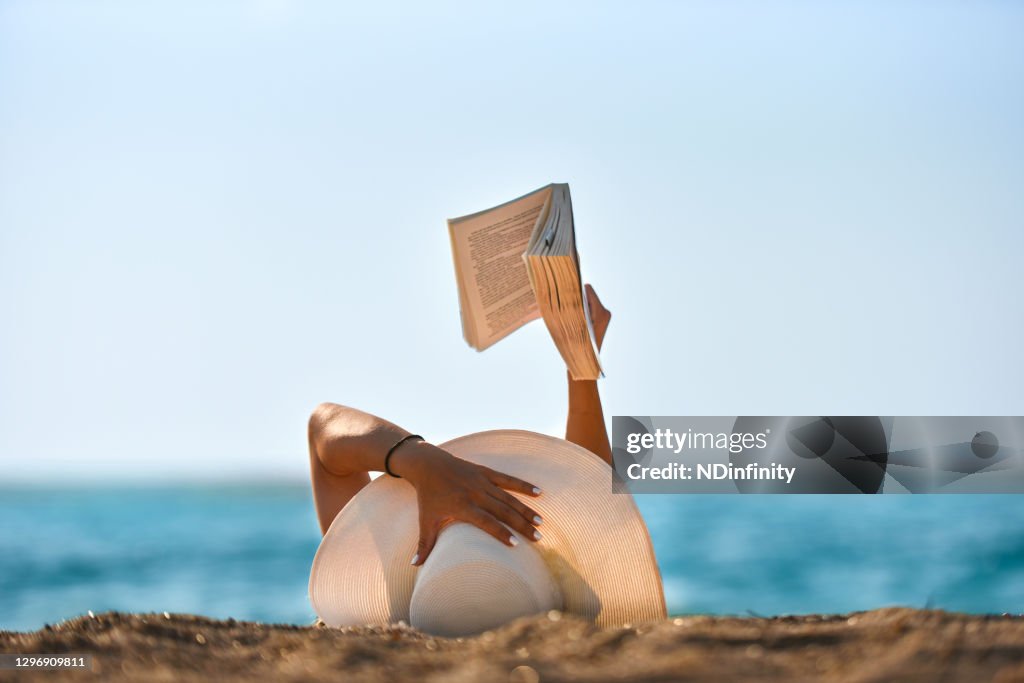 De jonge vrouw leest een boek op de foto van de strandvoorraad